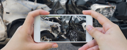 Woman taking a photo of damaged vehicles with her phone following a car accident