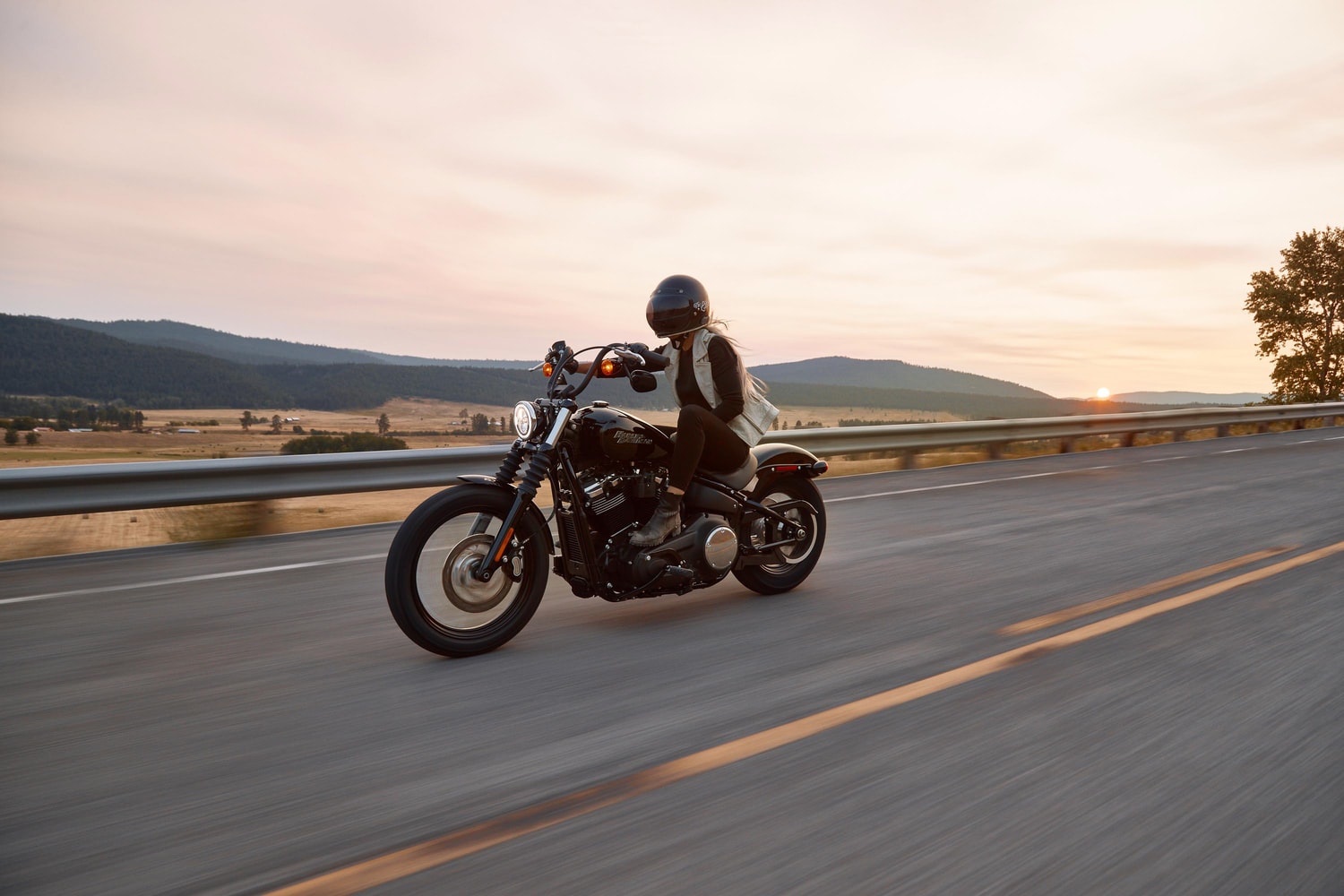 Motorcycle driving on highway with sun setting and mountains in the background