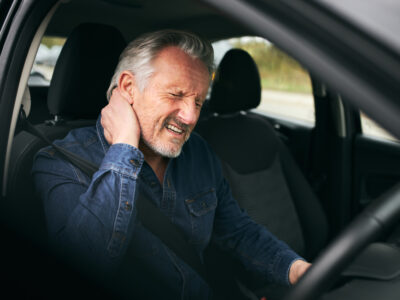A graying man in the driver' seat of his car holding his neck.